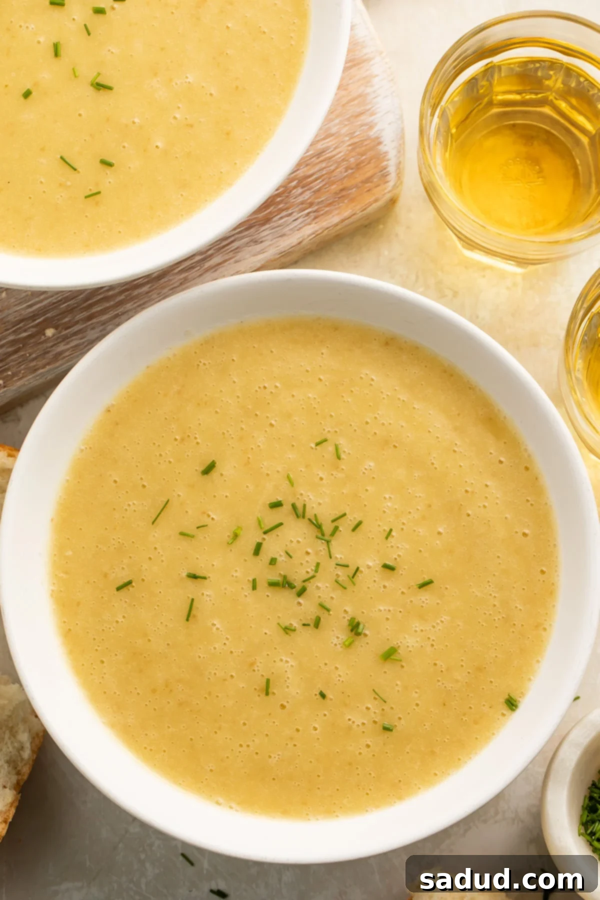 Bowls of yellow, creamy potato leek soup cooked in an Instant Pot on a table top with pieces of crusty bread surrounding.