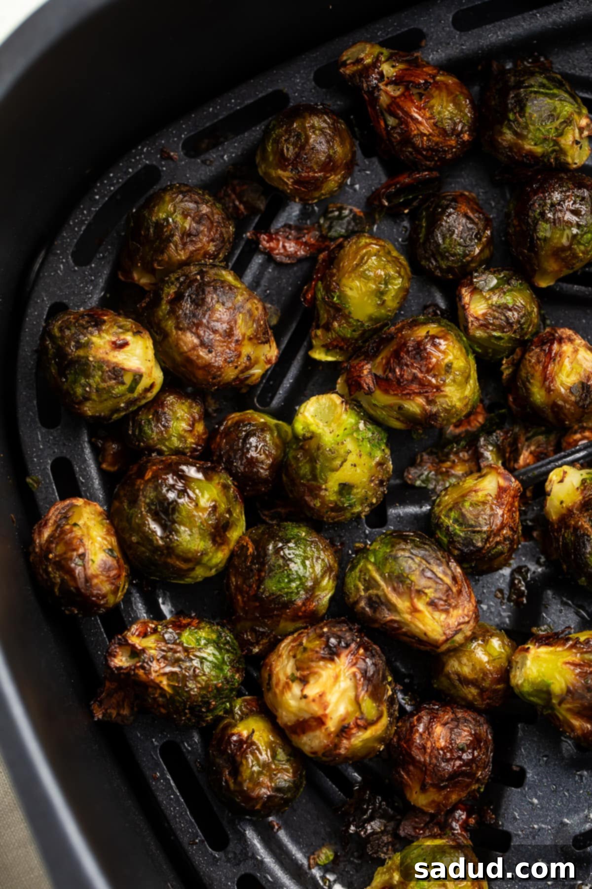 Frozen Brussels sprouts tossed with oil, salt, and pepper in an air fryer basket.