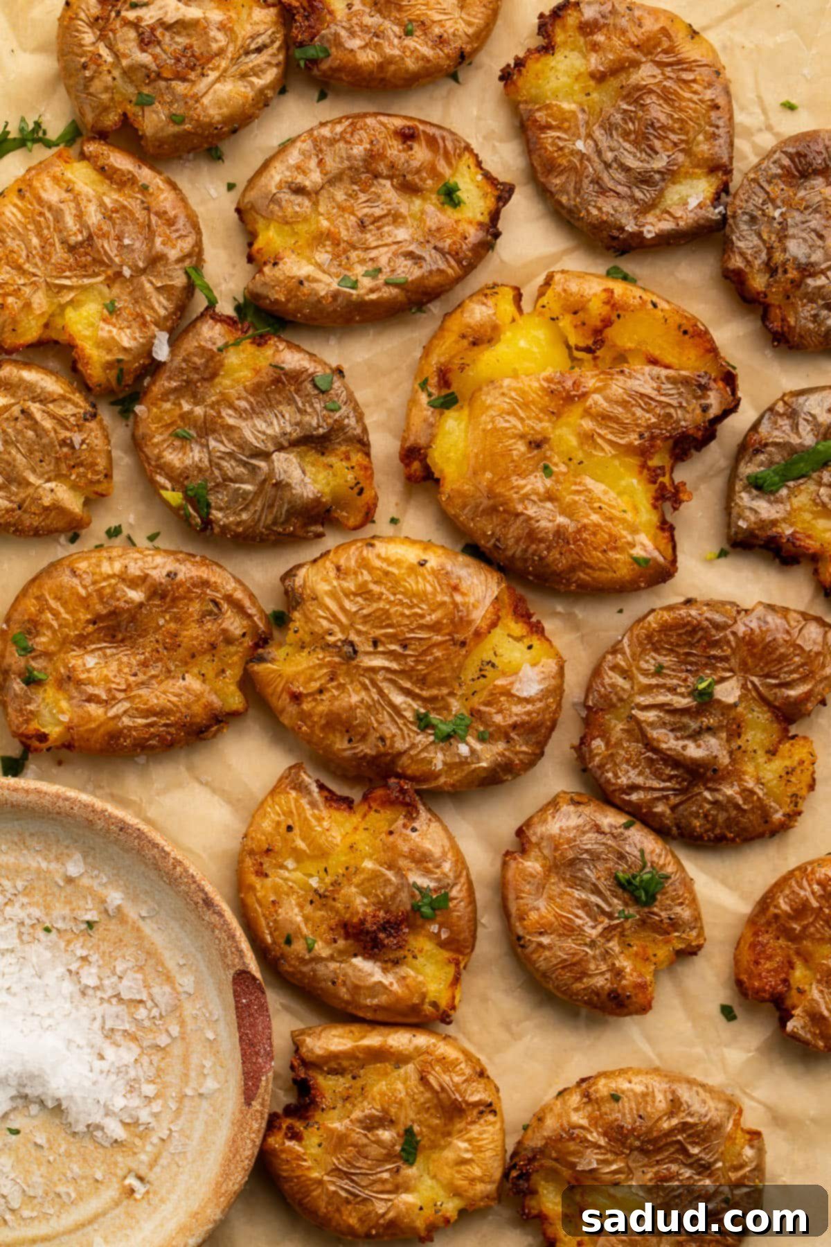 Multiple smashed potatoes, cooked in the air fryer, arranged on a sheet of parchment paper next to a small dish of salt.