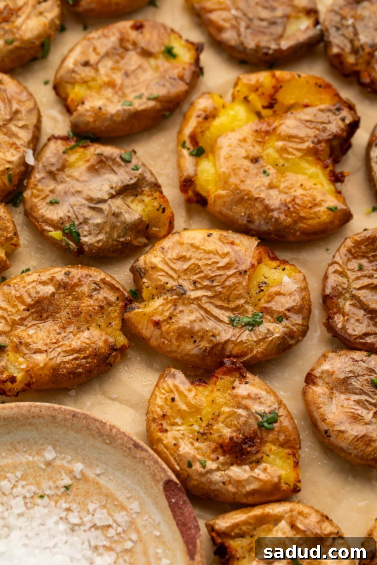 Multiple smashed potatoes, cooked in the air fryer, arranged on a sheet of parchment paper next to a small dish of salt.