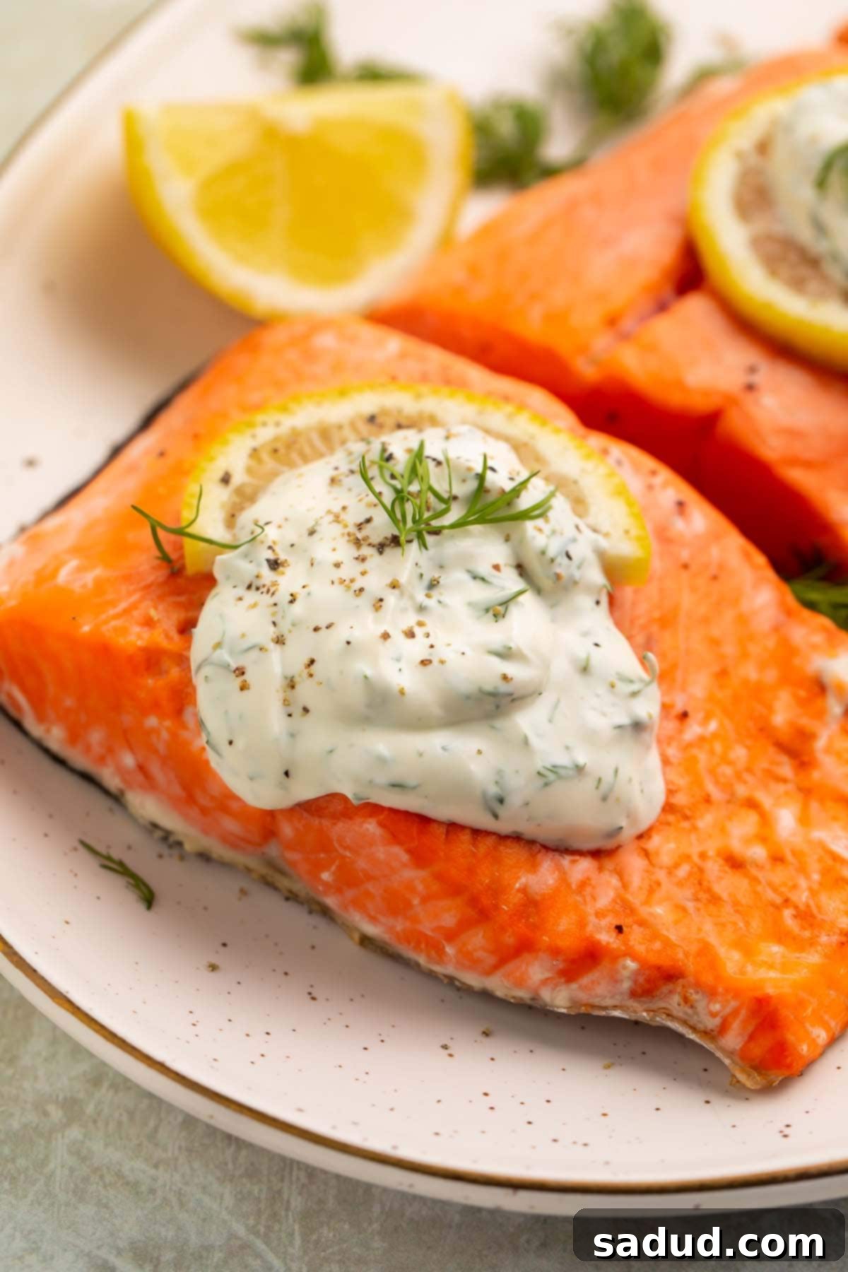A dollop of creamy dill sauce plopped on top of a salmon fillet with a thin lemon wedge.