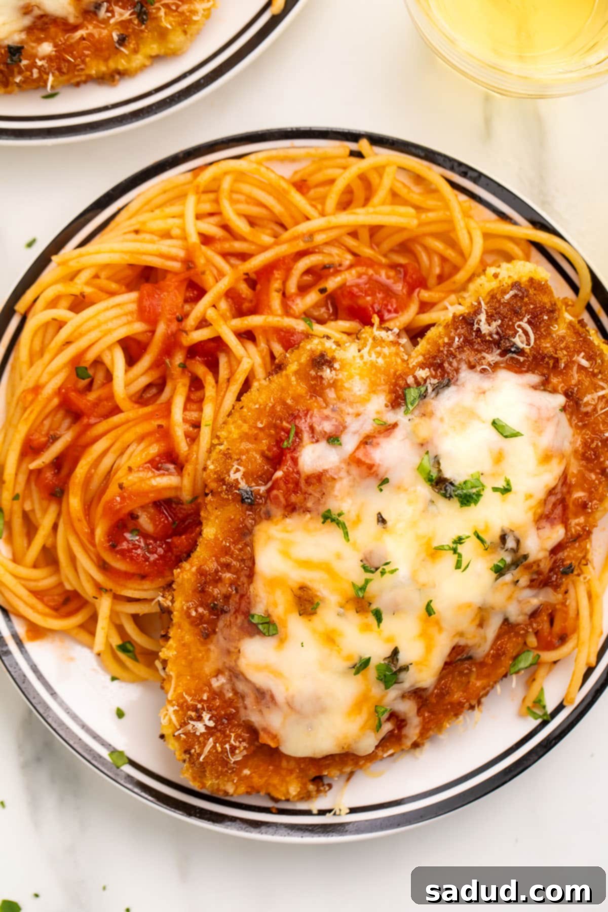 Gluten free chicken parmesan on a large plate with gluten free spaghetti and tomato sauce.