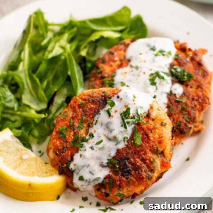 Quick Salmon Patties with Zesty Lemon Garlic Cream Sauce 4 Two salmon patties topped with lemon-garlic sauce on a plate with a small salad.