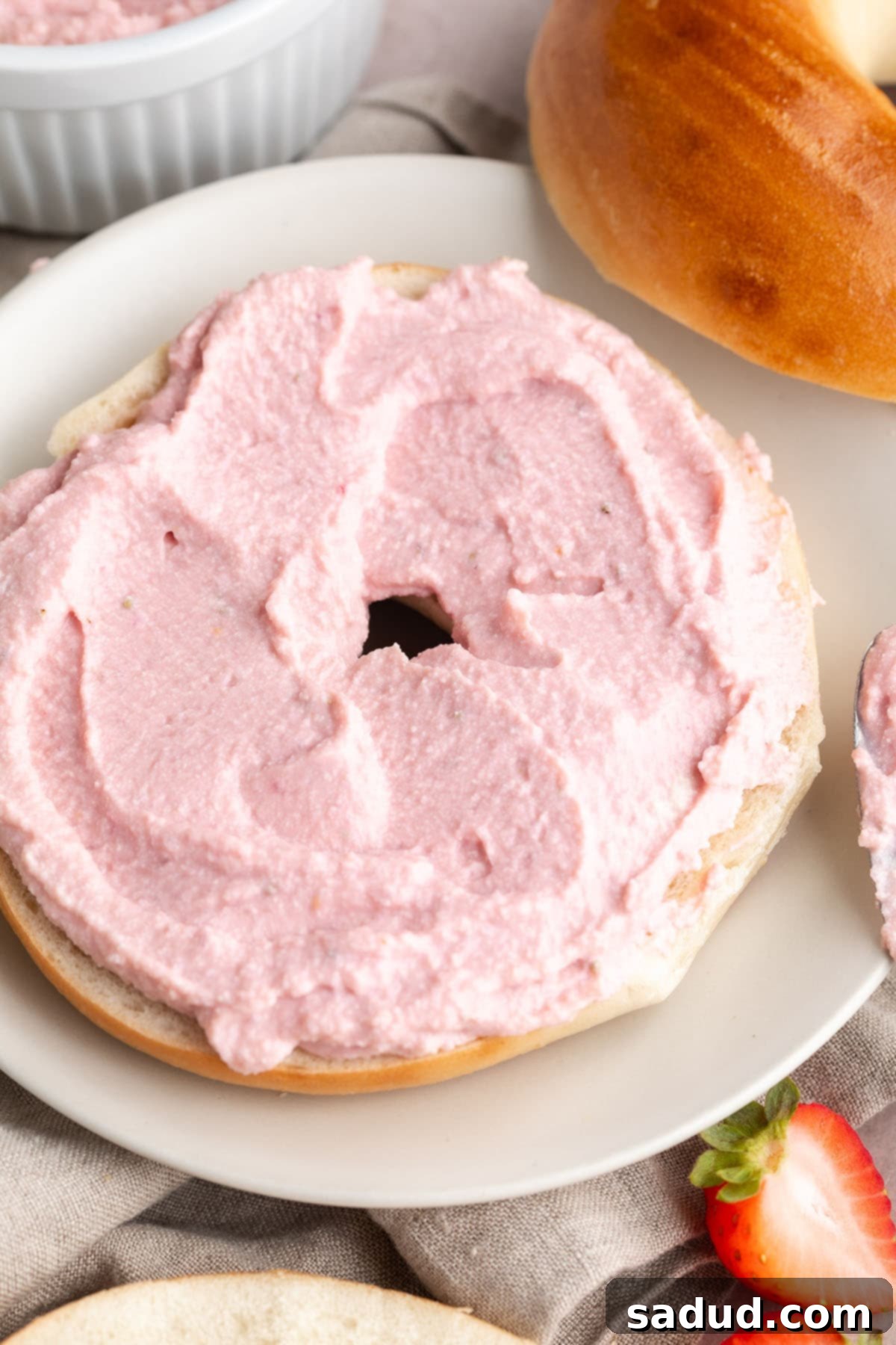 Mixed berry tofu cream cheese spread thickly on top of the bottom half of a bagel.