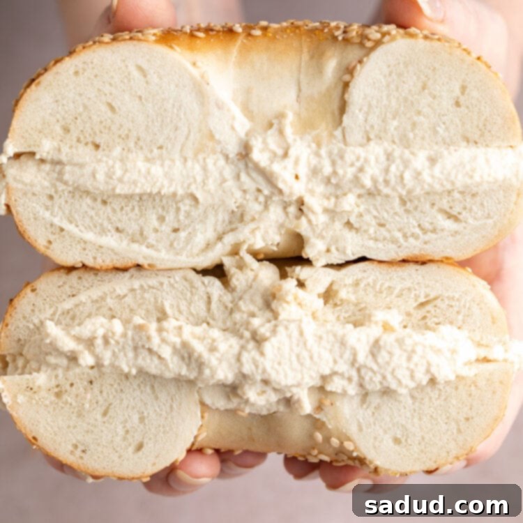 Thick layers of tofu cream cheese sandwiched between two bagel halves, stacked on top of each other.