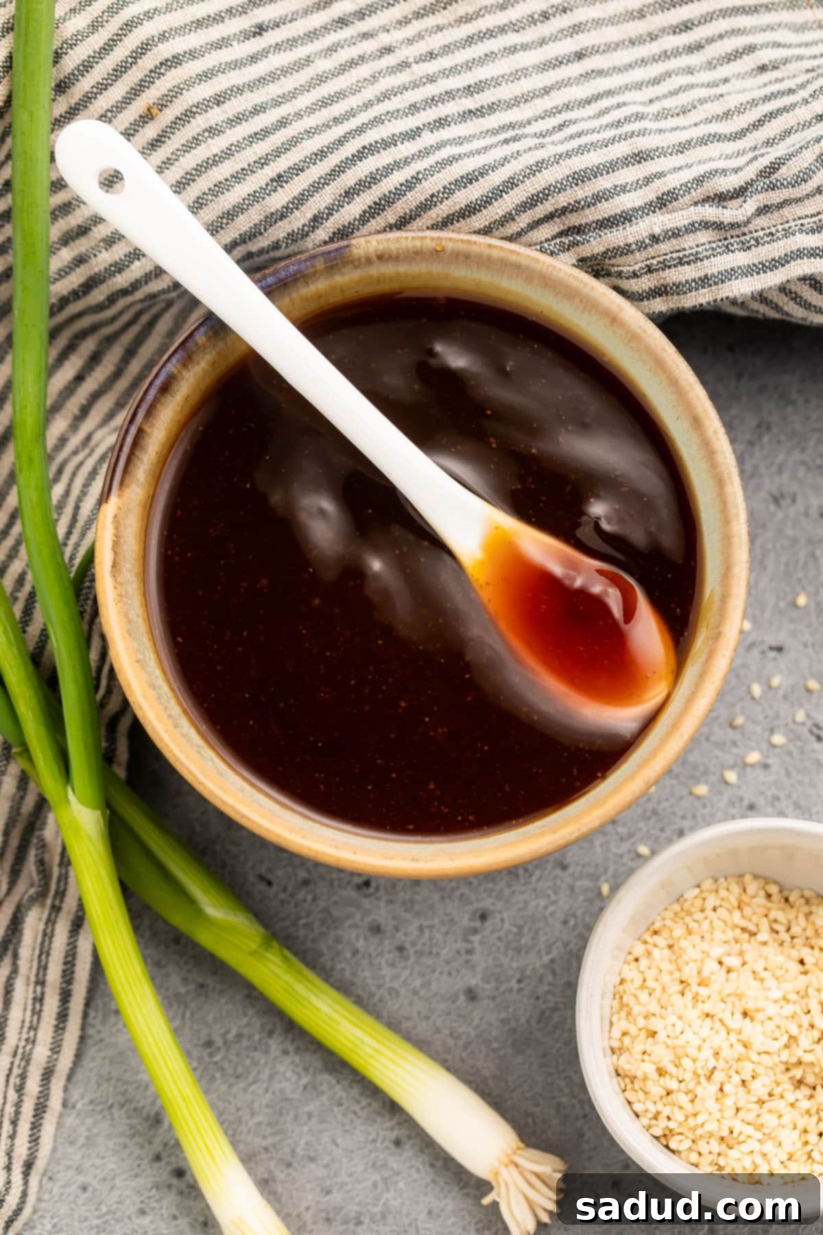 Overhead view of a bowl of rich, brown gluten free teriyaki sauce with a white spoon resting in the bowl, ready to be served.