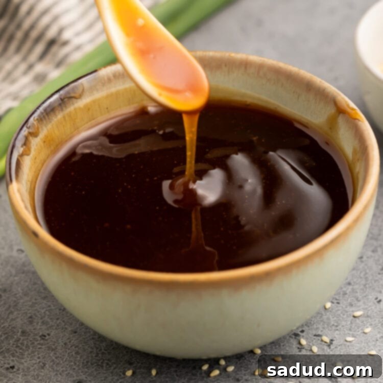 Gluten free teriyaki sauce being poured off a small white spoon into a bowl of teriyaki sauce, showcasing its perfect consistency.