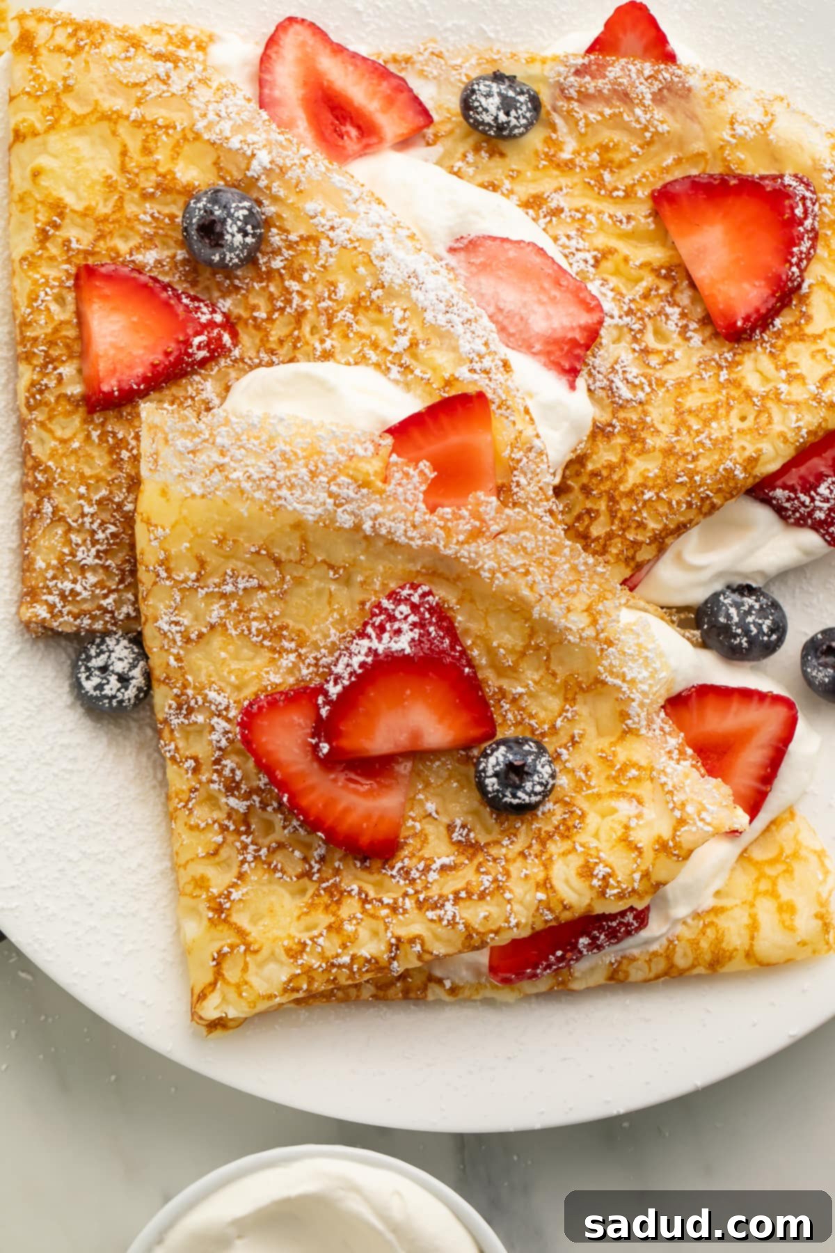Close up of a gluten free crepe on a plate with fresh blueberries and sliced strawberries.