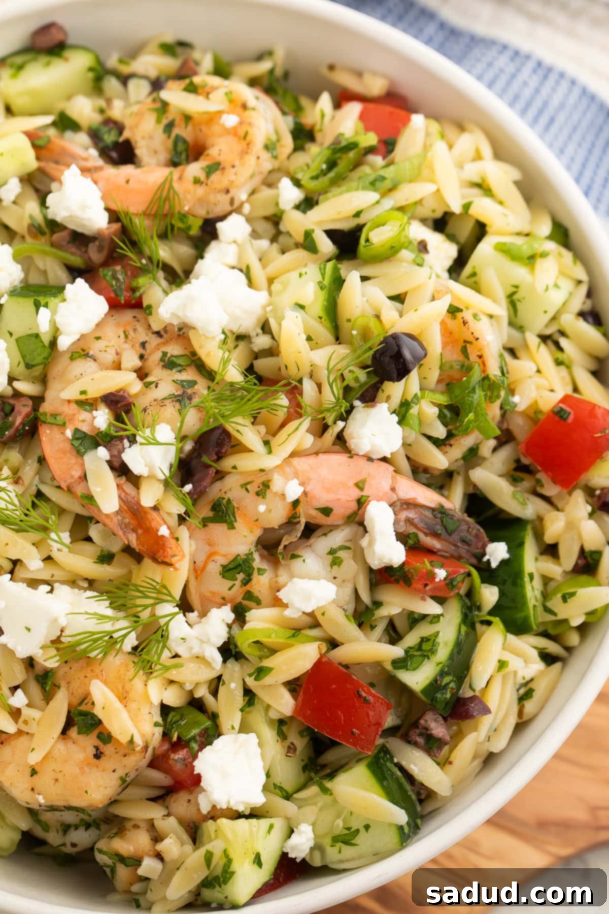 Close-up of a vibrant bowl of Greek shrimp orzo salad with feta, olives, and fresh herbs.