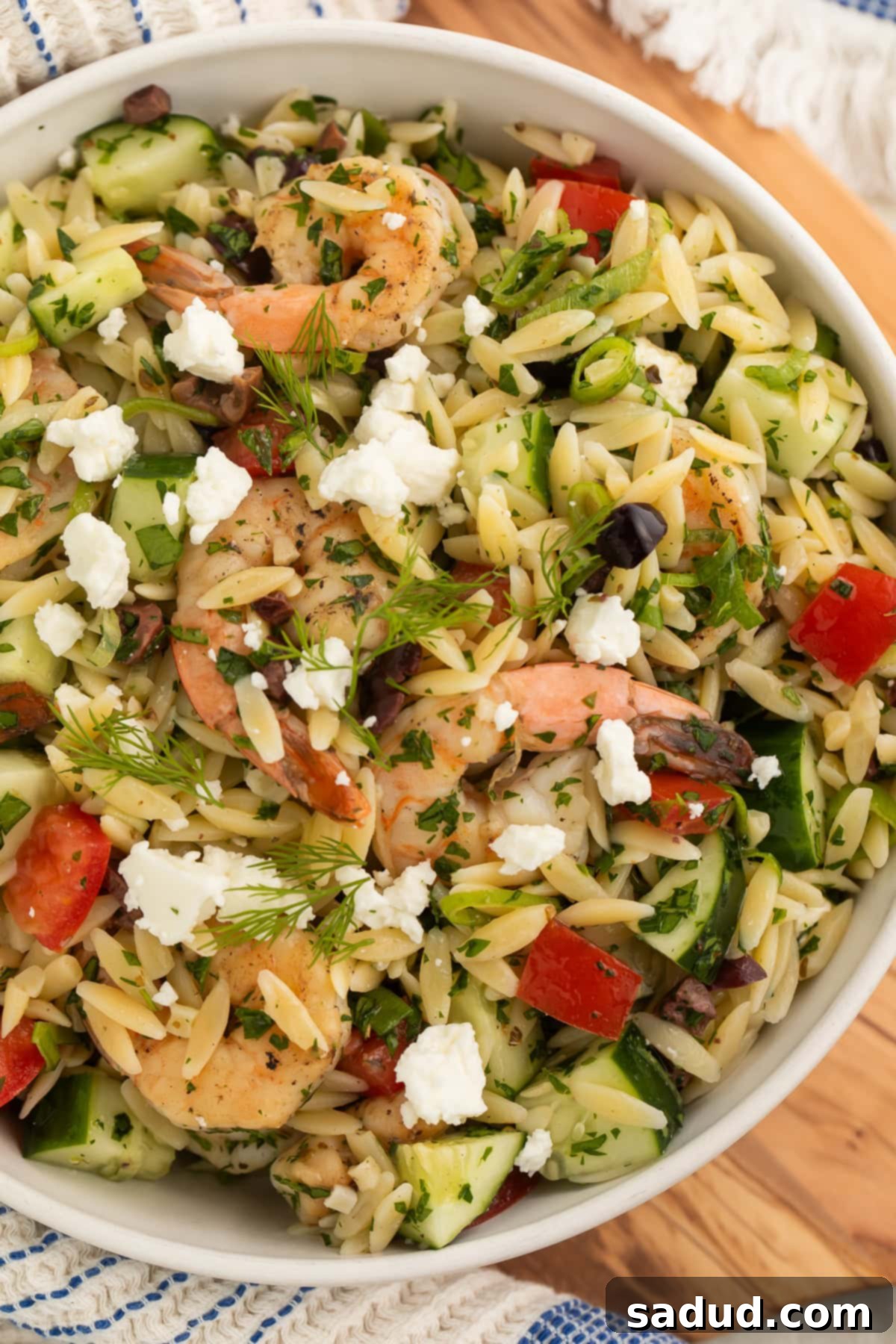 Close-up of a bowl of Greek shrimp orzo salad with vibrant vegetables and crumbled feta.