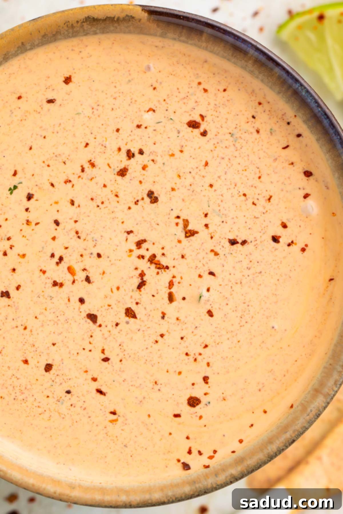 Close-up of a vibrant, peach-colored Southwest salad dressing, artfully garnished with a sprinkle of smoked paprika, presented in a sleek medium-sized bowl.