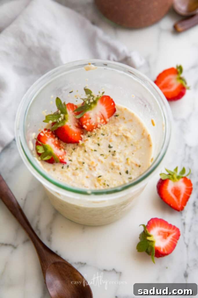 Classic strawberry vegan overnight oats in a glass jar, topped with fresh strawberries and a hint of mint.