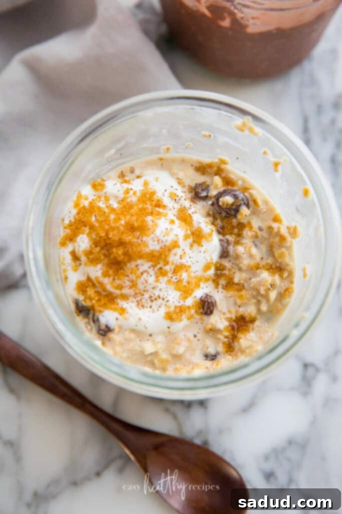 Warm and inviting cinnamon raisin vegan overnight oats, topped with a dollop of yogurt, extra raisins, and a dusting of cinnamon.