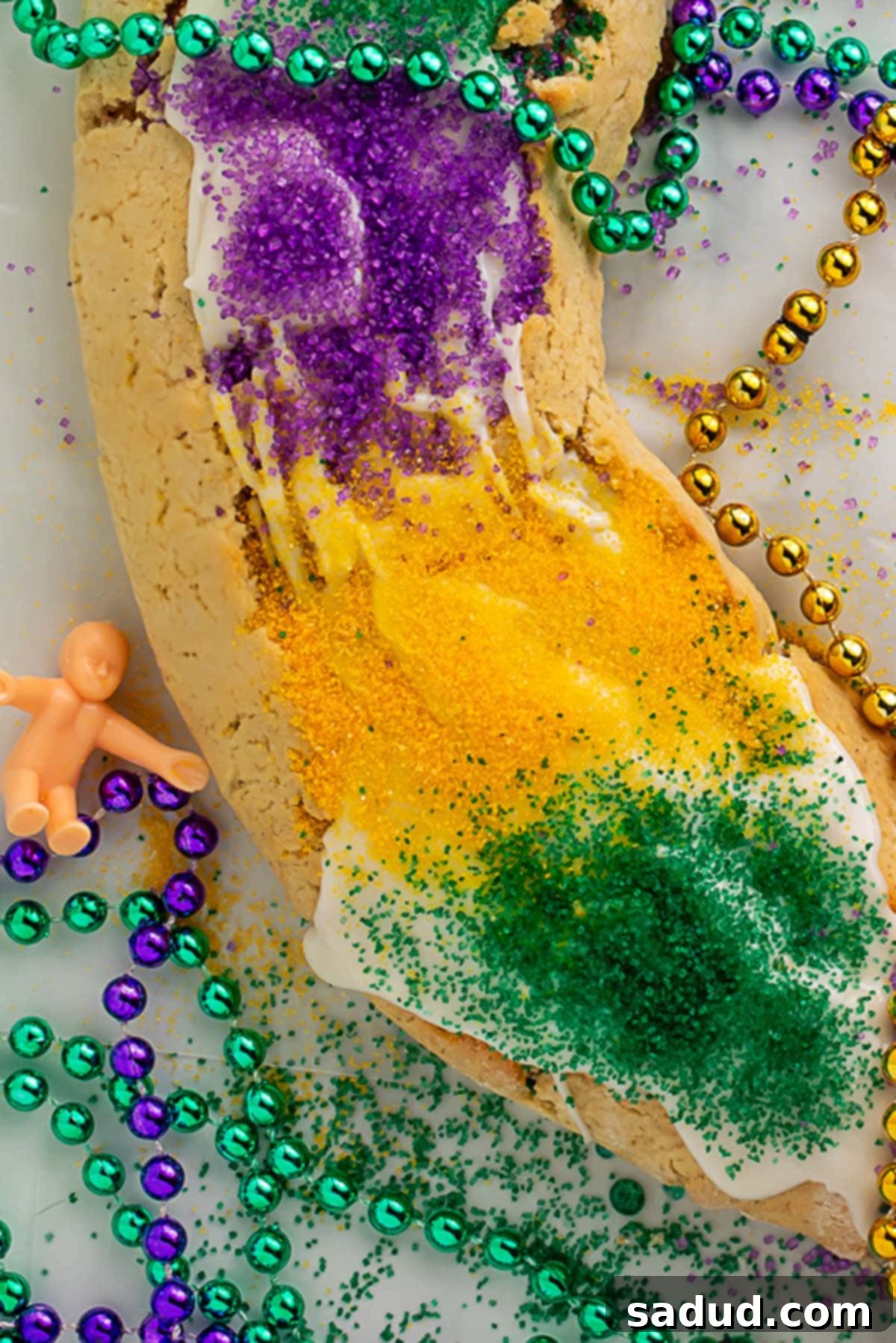 Close-up photograph of a small plastic King Cake baby resting beside a slice of gluten-free King Cake.