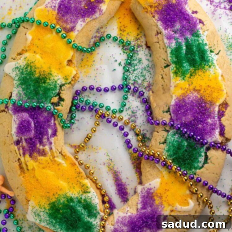 A large oval-shaped gluten free king cake topped with purple, yellow, and green sanding sugar and surrounding by purple, gold, and green Mardi Gras bead necklaces.