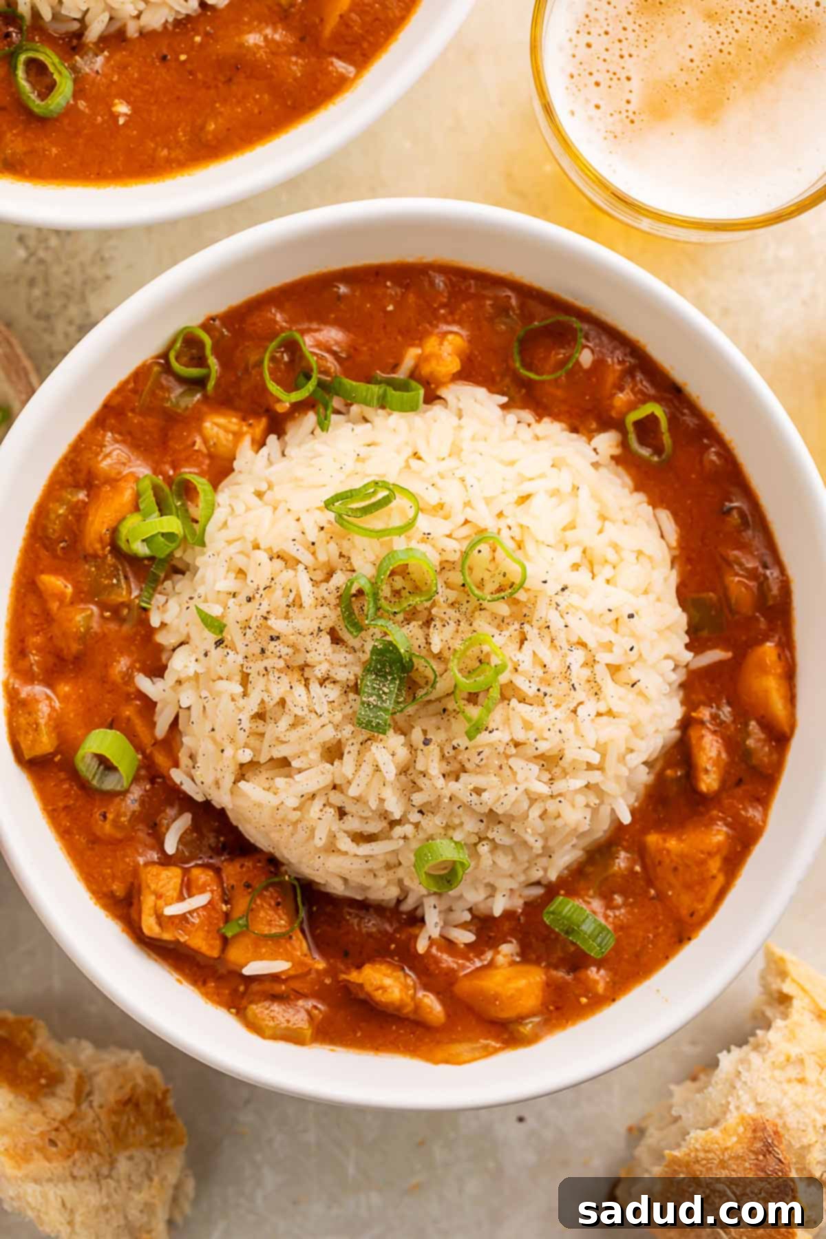 Southern Comfort Chicken Etouffee 2 A bowl of chicken etouffee, topped with a large scoop of rice, on a table surrounded by pieces of crusty bread.
