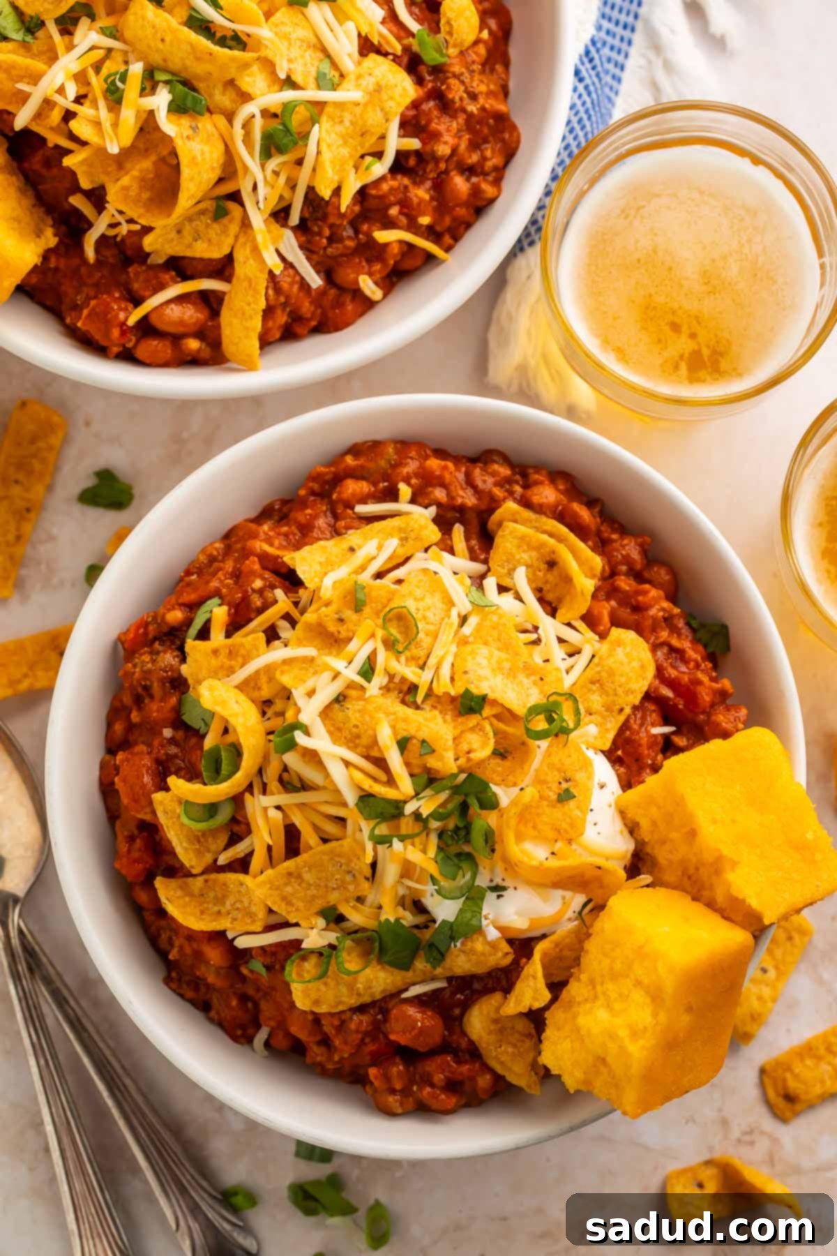 Two bowls of the hearty Boilermaker Chili, generously topped with crunchy corn chips and served alongside two pieces of golden cornbread, expertly photographed from an overhead perspective, showcasing the delicious toppings and inviting presentation.