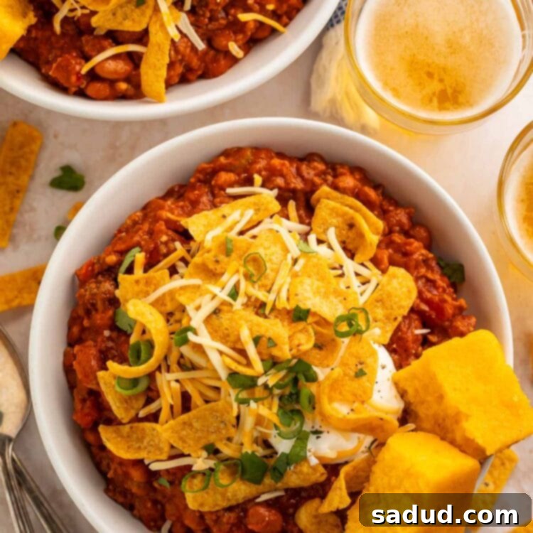 A top-down view of two hearty bowls of Boilermaker Chili, garnished with crispy corn chips and flanked by golden squares of cornbread, ready to be served.