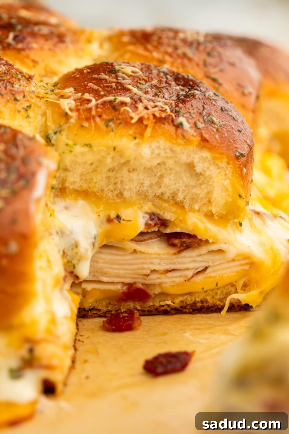 A chicken bacon ranch slider photographed from the side to show the layers of deli chicken, bacon, cheese, and ranch dressing.