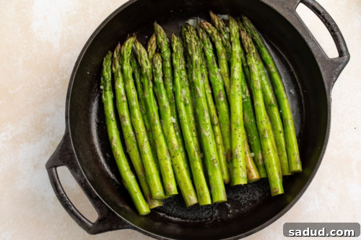 Close-up of tender, smoked asparagus spears glistening in a large cast-iron skillet after cooking.
