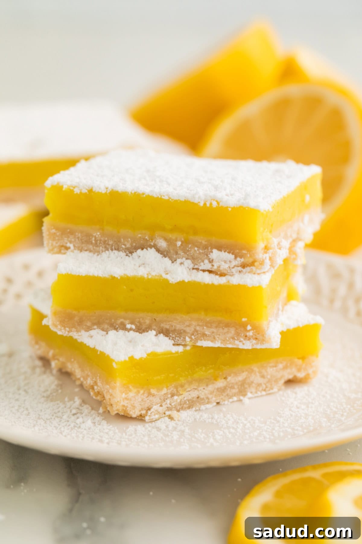 A stack of 3 vegan lemon bars, each topped with powdered sugar, on a white plate, ready to be served.