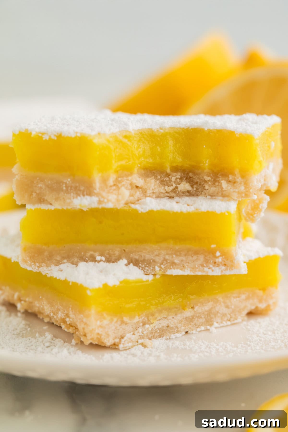 Close-up of a single vegan lemon bar, showing its rich yellow filling and shortbread crust, lightly dusted with powdered sugar.