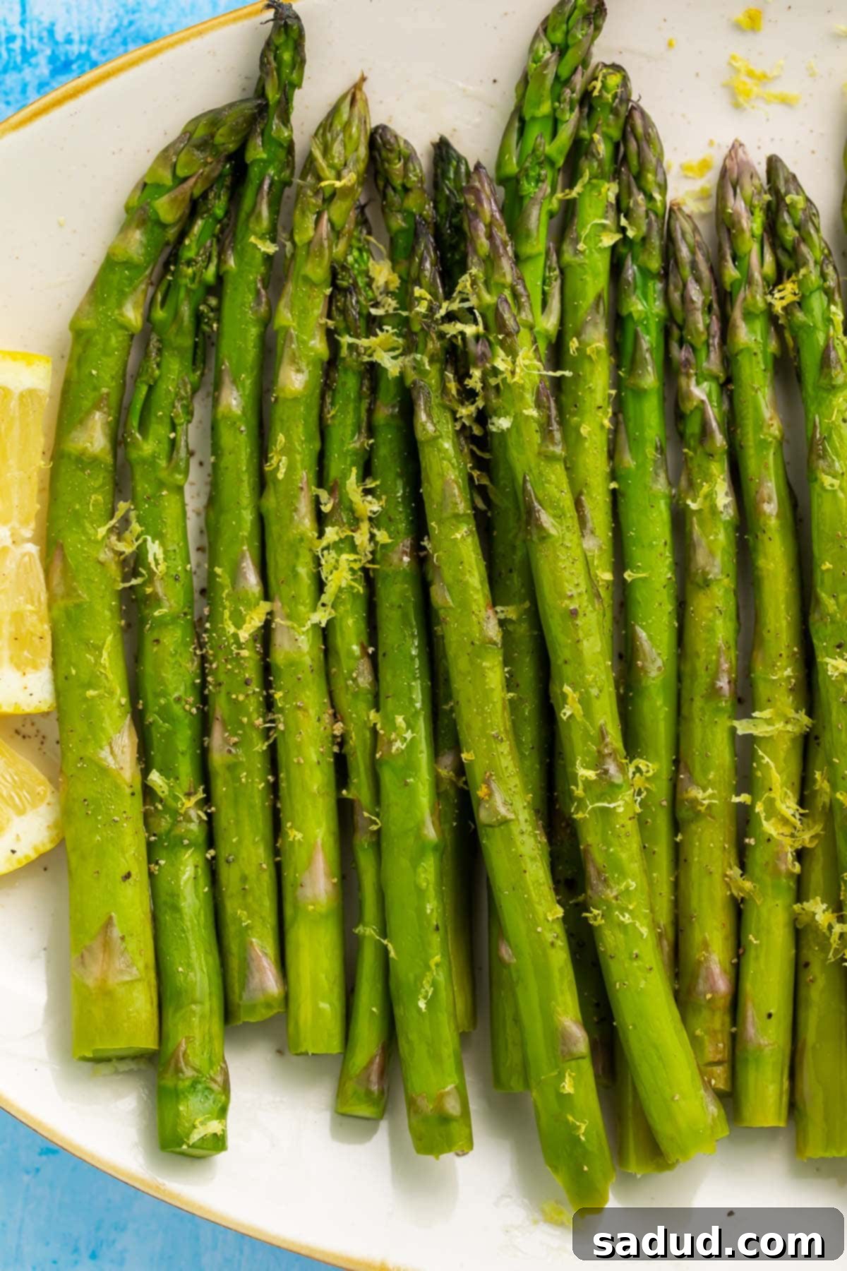 Asparagus, cooked in a sous vide, arranged on a white oval platter on a blue background.
