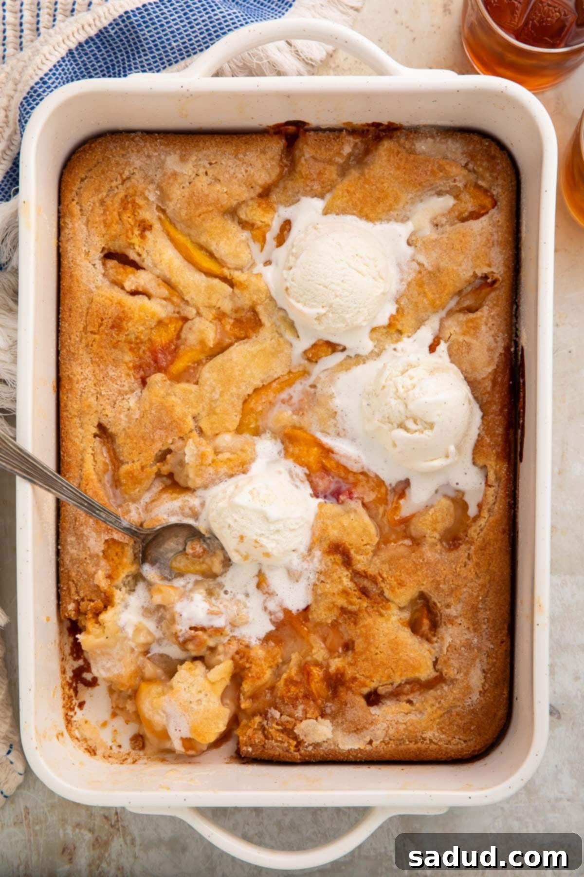 Overhead photo of a rectangular baking dish holding a gluten free peach cobbler topped with scoops of vanilla ice cream.