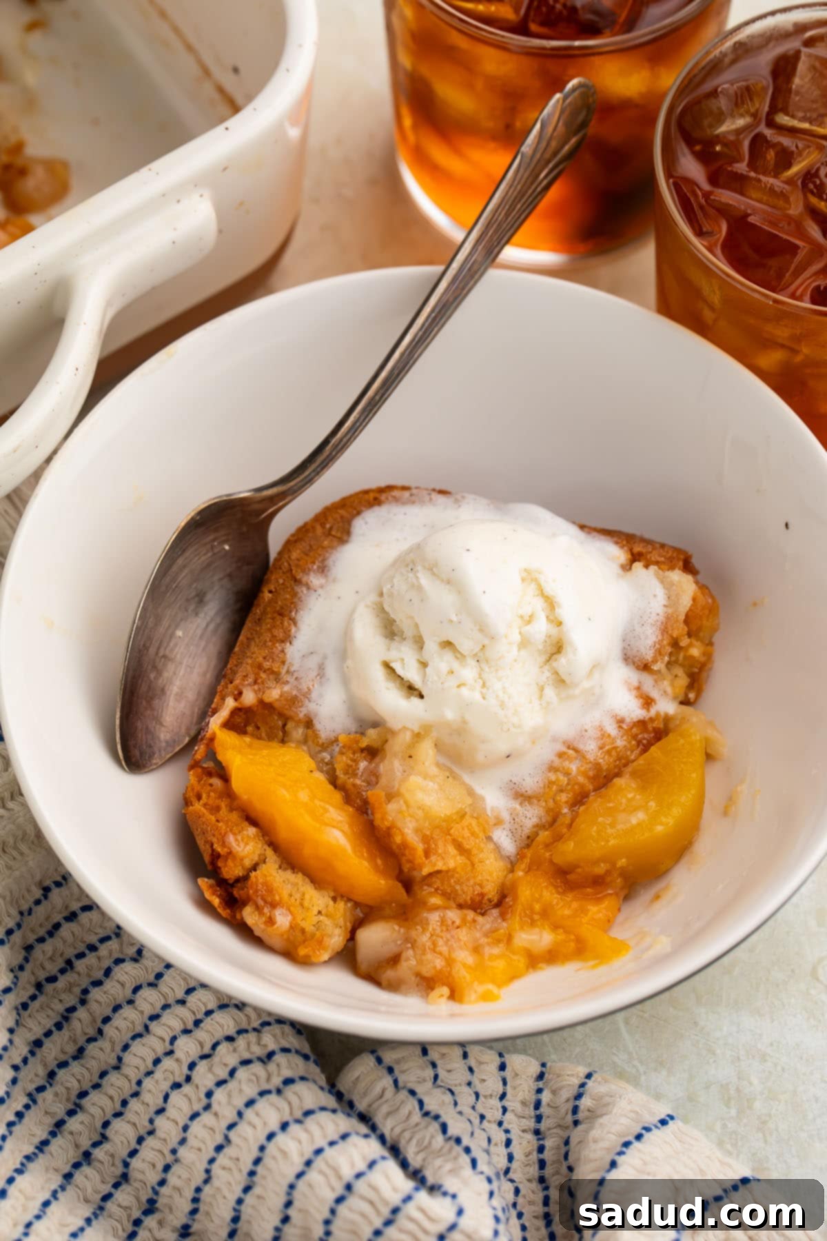A square of gluten free peach cobbler in a bowl, topped with a scoop of vanilla ice cream.