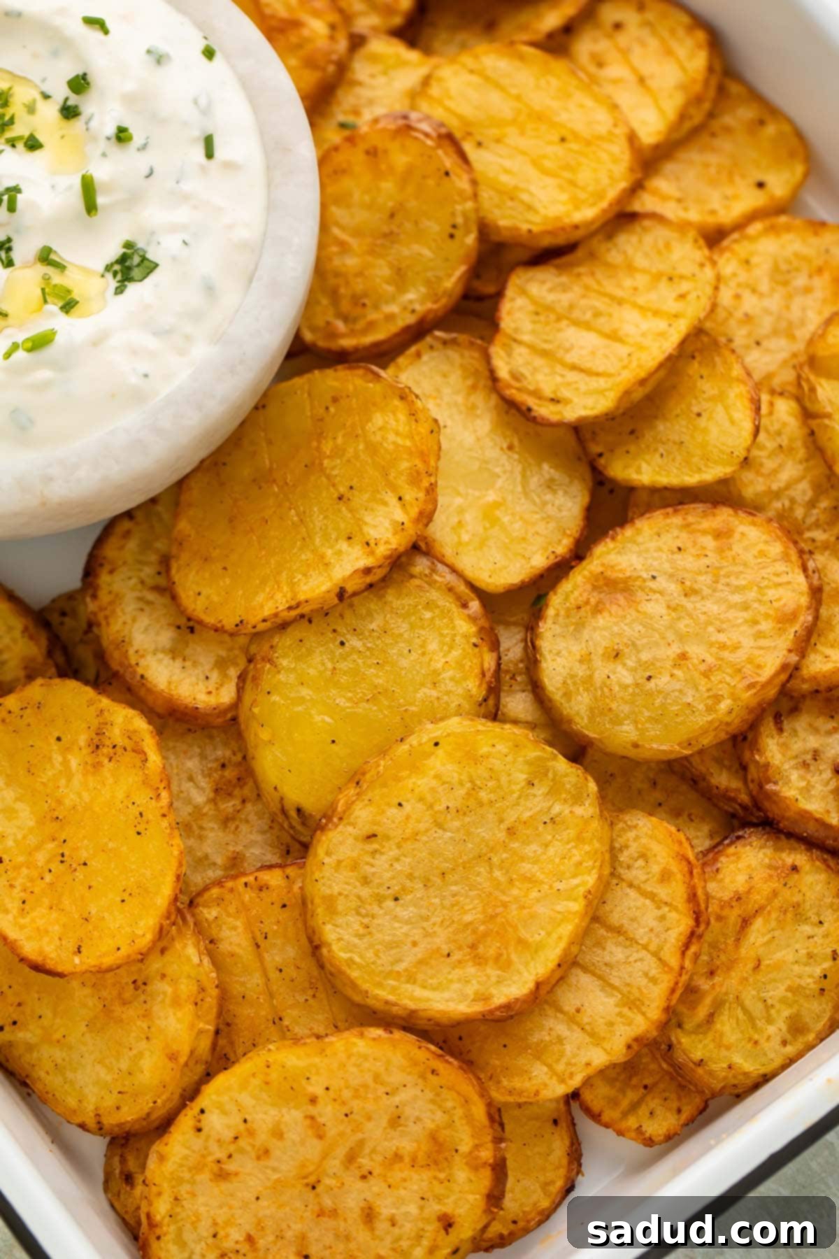 Close-up of thinly sliced, golden-brown crispy air fryer potatoes on a serving tray with a small bowl of creamy green herb dipping sauce.