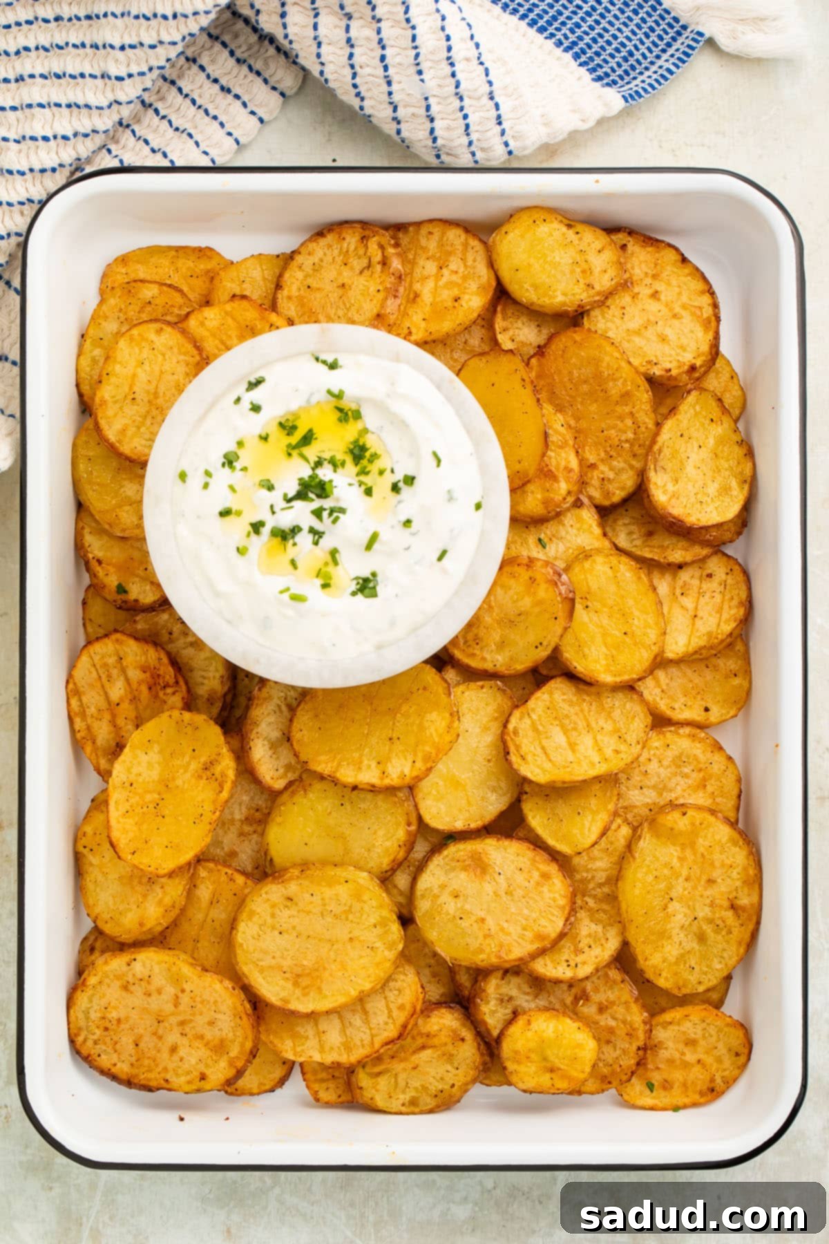 A wider shot of the tray of crispy air fryer sliced potatoes, with the creamy herb dipping sauce and a scattering of fresh herbs.