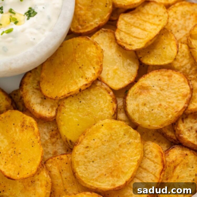 Close-up of golden-brown crispy air fryer sliced potatoes with a side of creamy herb dipping sauce.