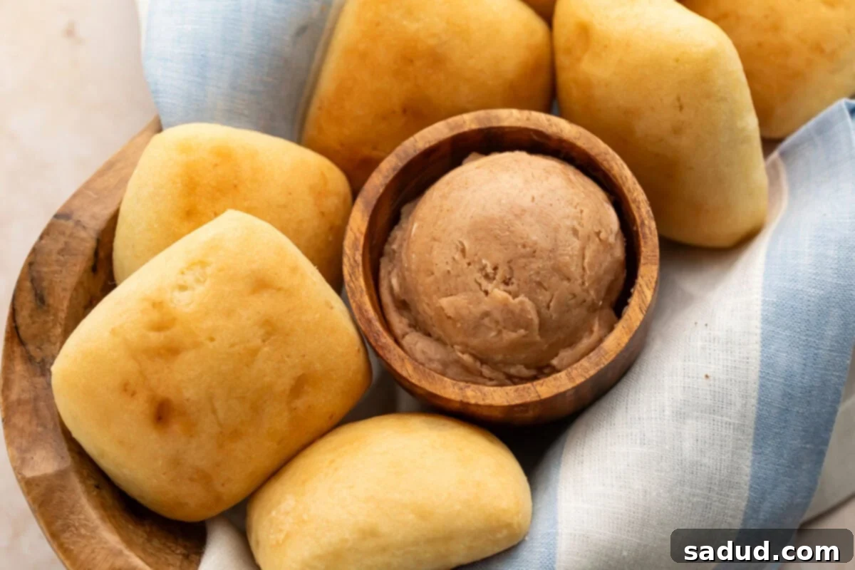 A small wooden bowl containing a scoop of rich brown Texas Roadhouse cinnamon honey butter nestled in a basket with golden yeast rolls.