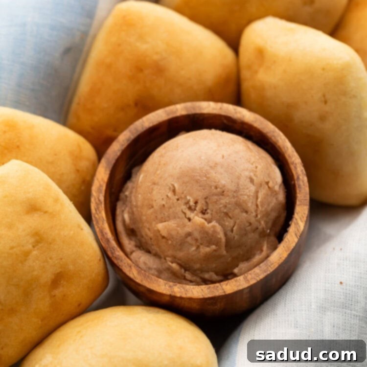 A small wooden bowl containing a scoop of rich brown Texas Roadhouse cinnamon honey butter nestled in a basket with golden yeast rolls.