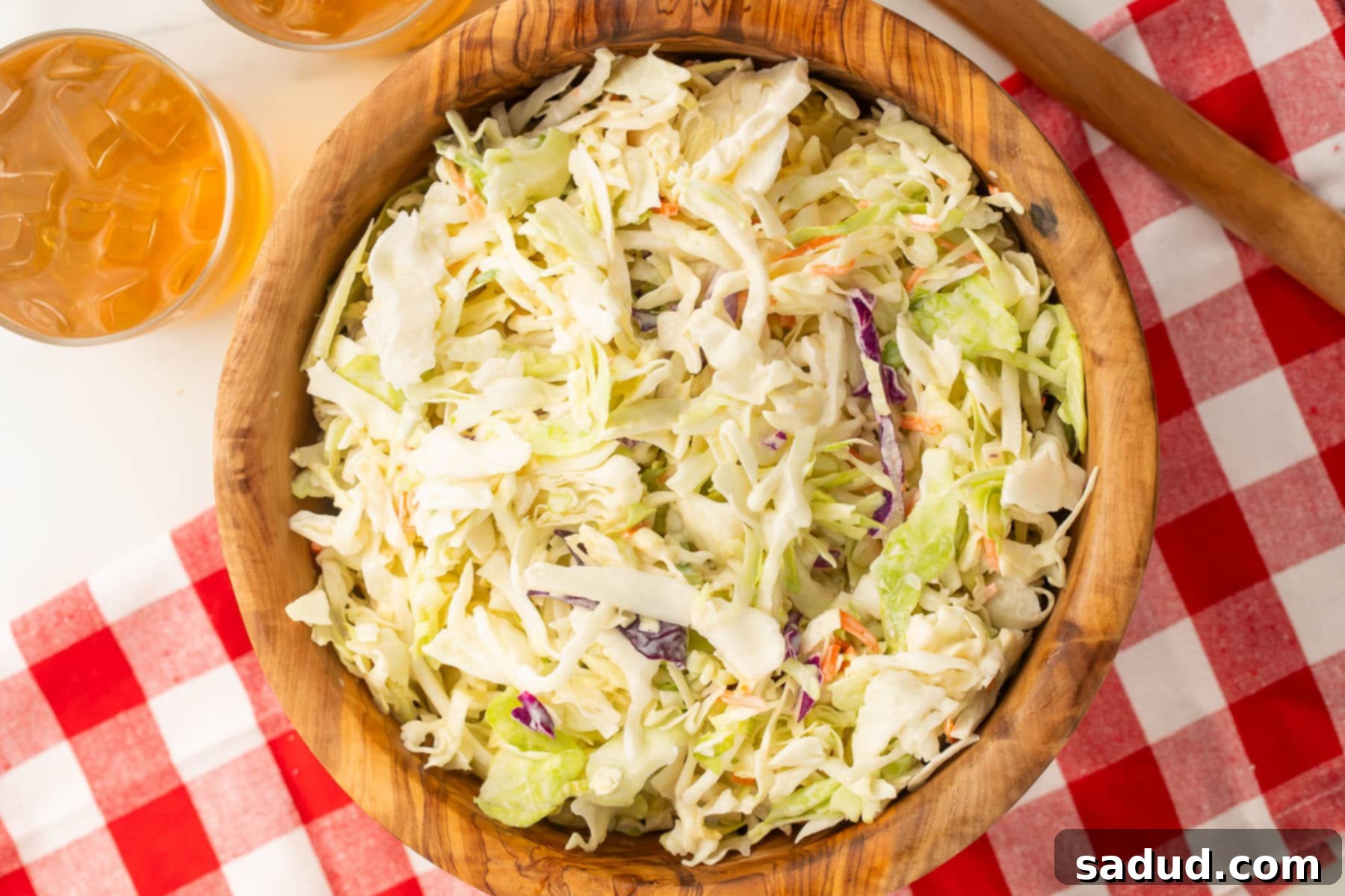 A large wooden bowl filled with creamy vegan coleslaw, placed on a picnic table covered with a red and white checkerboard tablecloth, ready for serving at a summer gathering.