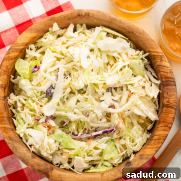 A wooden bowl containing creamy vegan coleslaw sits on a table partially covered by a red and white checkerboard tablecloth, highlighting its fresh appeal.