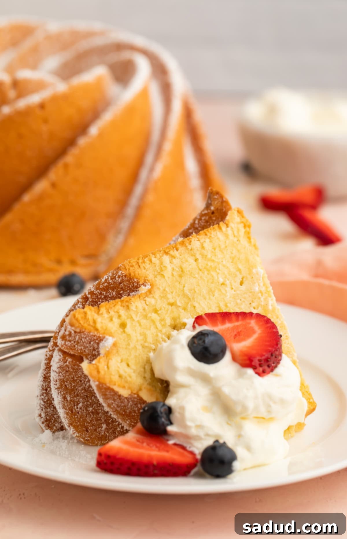 A perfectly sliced piece of Gluten Free Pound Cake served on a small dessert plate, garnished with fresh whipped cream and an assortment of juicy berries.