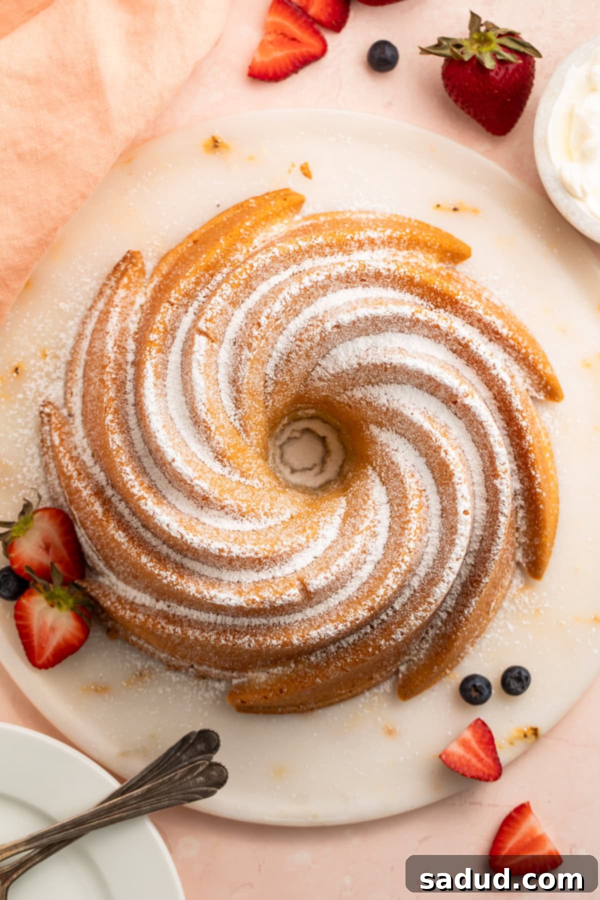An inviting overhead photo showcasing a beautifully baked gluten-free pound cake, artfully arranged on a platter with an abundance of fresh, colorful berries surrounding it.