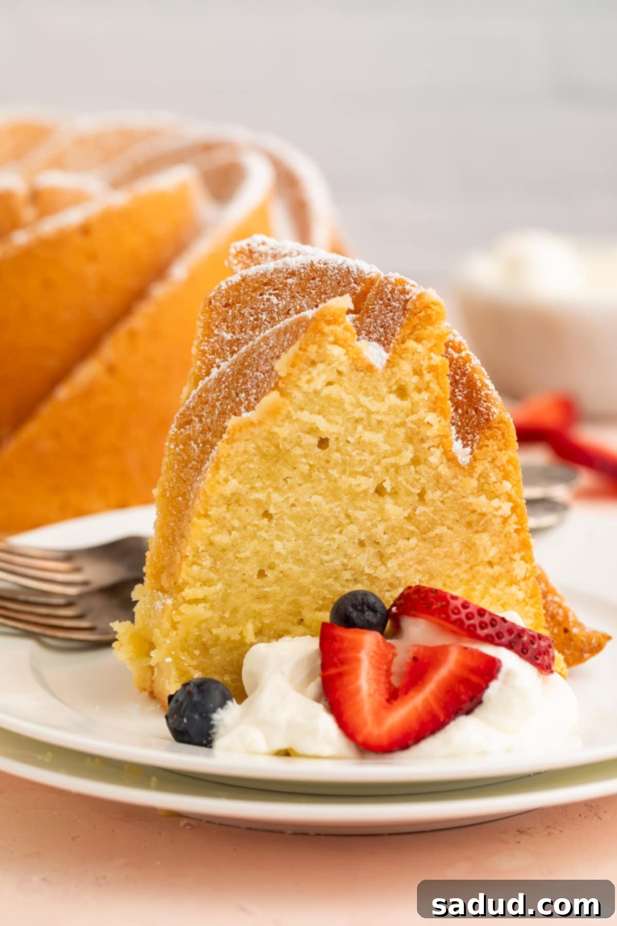 A delectable slice of Gluten Free Pound Cake presented on a dainty small dessert plate, elegantly topped with fluffy whipped cream and a scattering of vibrant fresh berries.