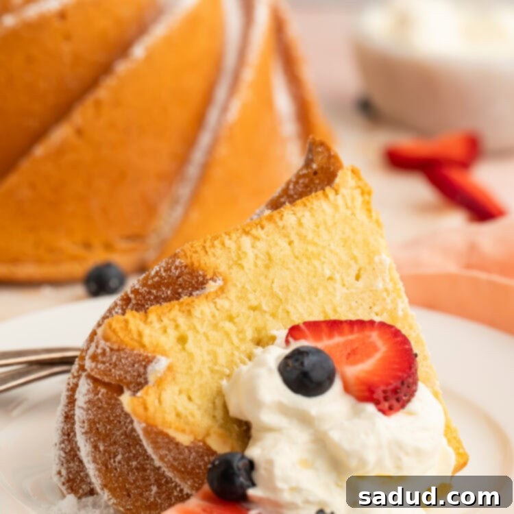 A close-up shot of a perfectly baked gluten-free pound cake slice, artfully presented on a small dessert plate and accompanied by a dollop of fresh whipped cream and an assortment of vibrant berries.