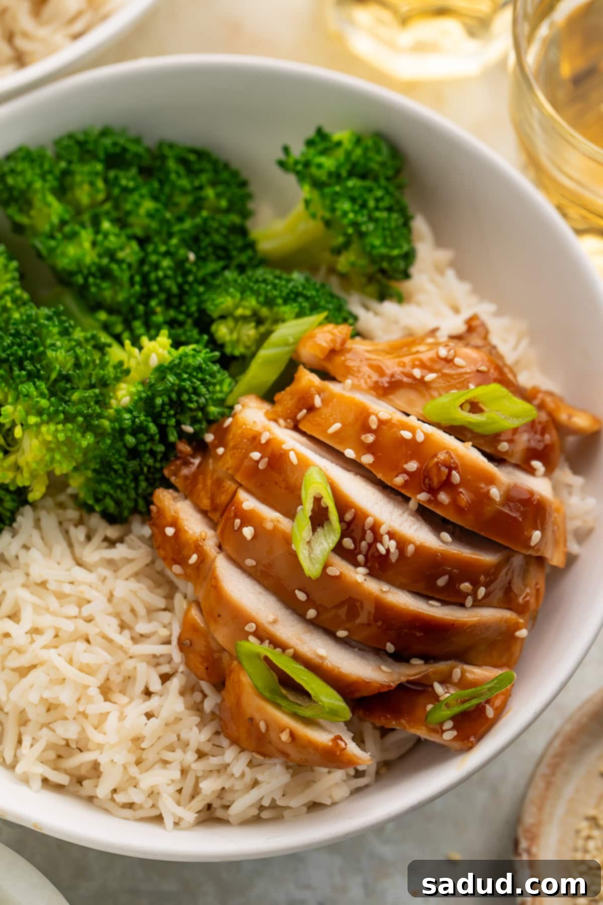 Sliced teriyaki chicken breast in a white bowl with brown rice and steamed broccoli. 