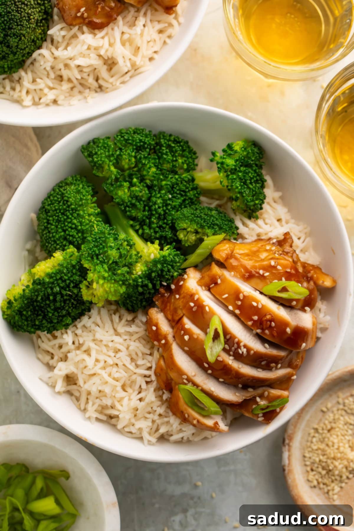 Bowls of rice, broccoli and sliced teriyaki chicken with glasses of beer visible off to the side. 