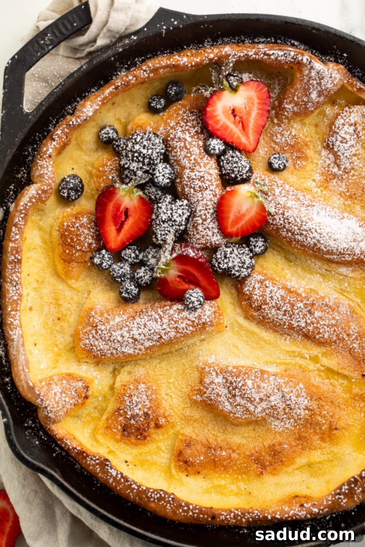 Close up of a dutch baby with strawberries and blueberries in a cast iron skillet.