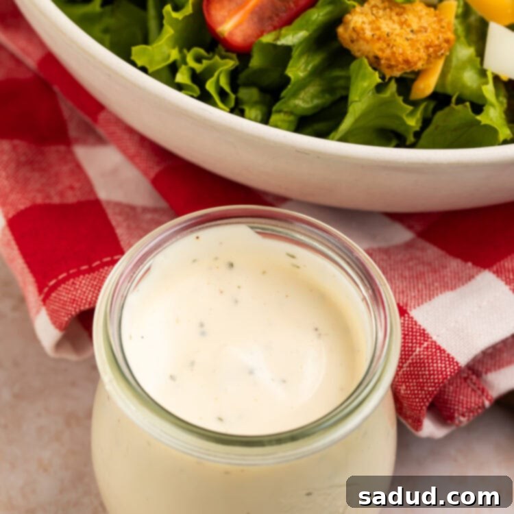 Glass jar of ranch dressing with a bowl of salad in the background.