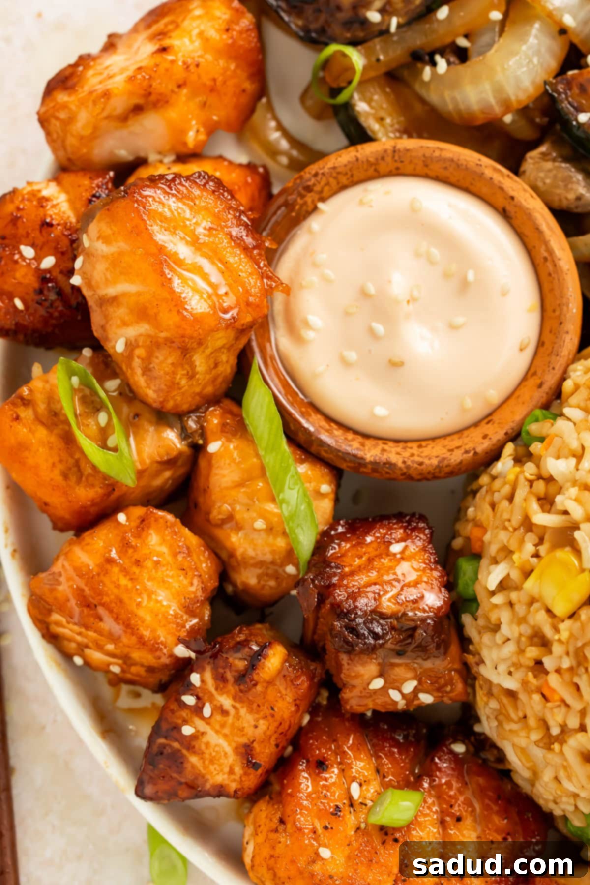 Close up of salmon hibachi bites on a plate with a pot of creamy dipping sauce.