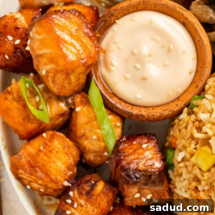 Close up of salmon hibachi bites on a plate with a pot of creamy dipping sauce.