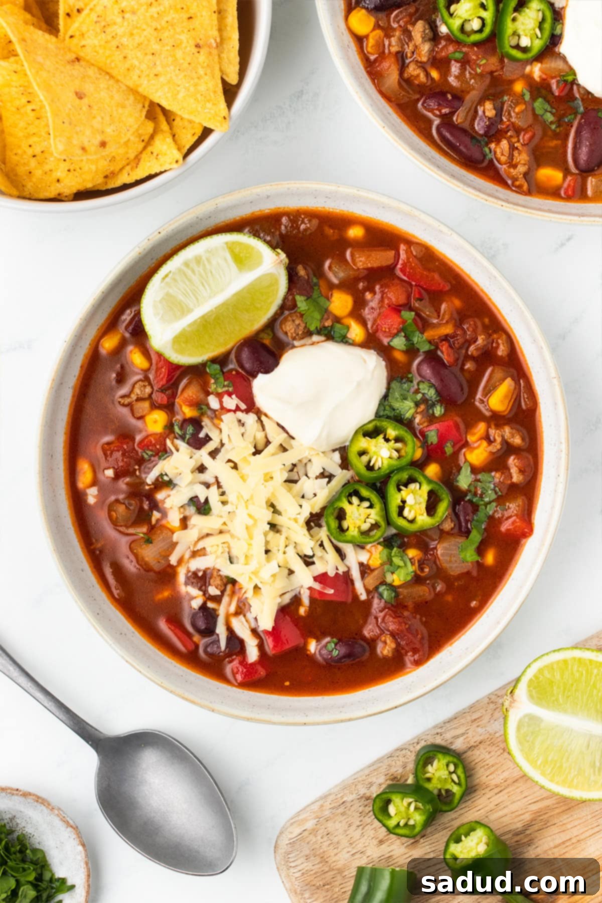 Bowl of chili topped with sour cream, shredded cheese, sliced jalapeños and a lime wedge.