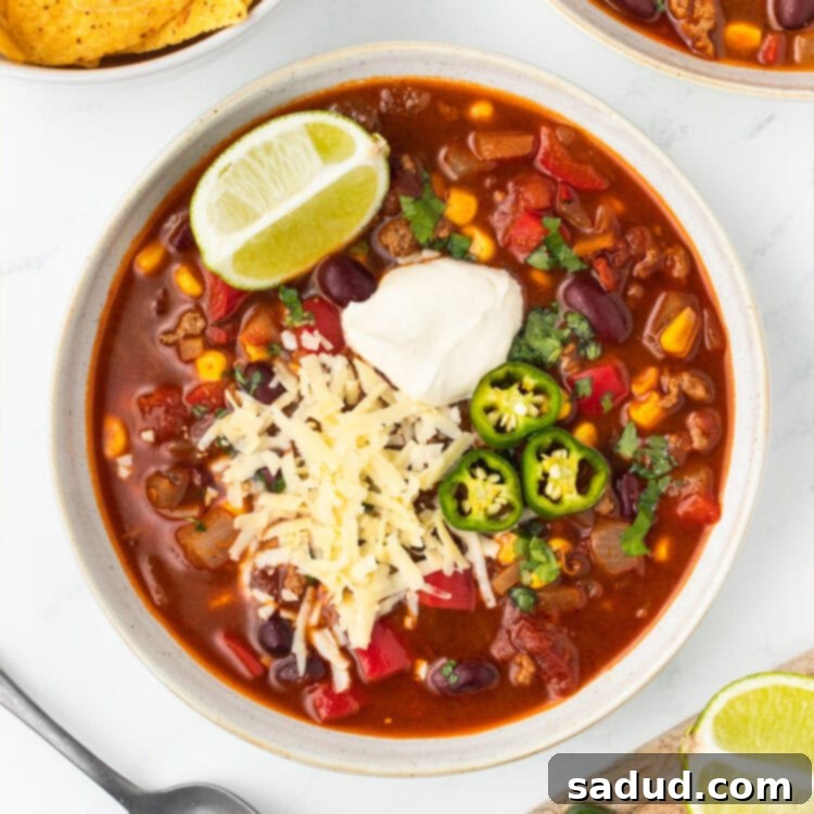 Bowl of chili topped with sour cream, shredded cheese, sliced jalapeños and a lime wedge.
