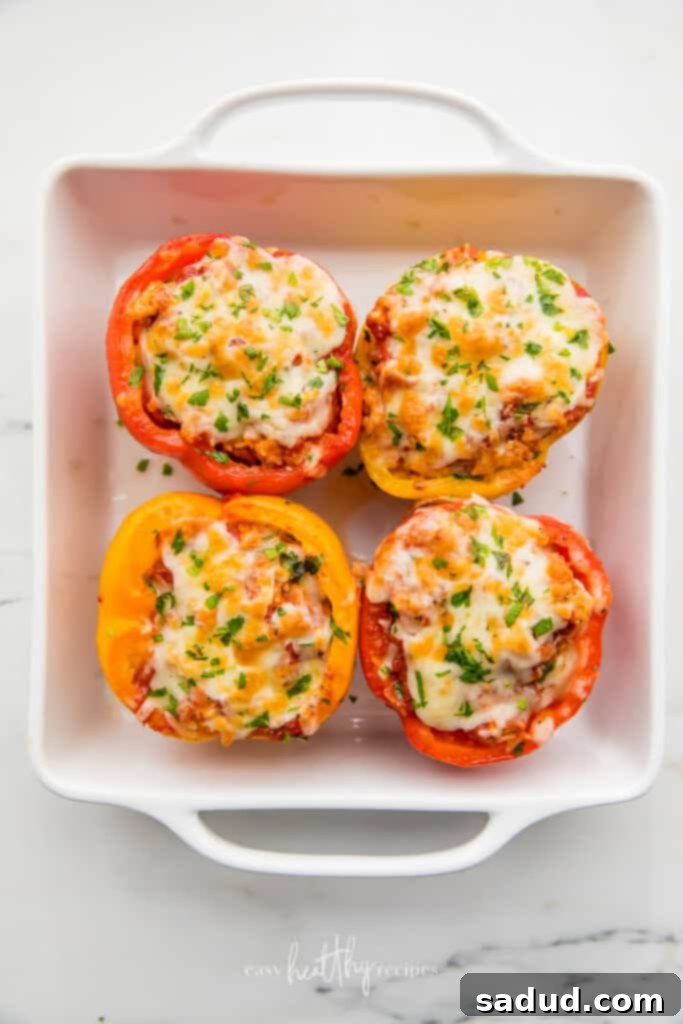 Close-up of baked Turkey Stuffed Peppers in a white baking dish, featuring golden melted mozzarella cheese and fresh green parsley garnish. Emphasizes the appetizing texture and vibrant colors.