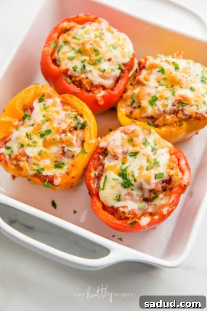Four perfectly baked Turkey Stuffed Peppers arranged in a white casserole dish, garnished with vibrant green parsley on top of melted mozzarella cheese. Ready to be served.